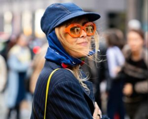 A woman in orange glasses, a denim cap and blue scarf